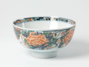  An ornate ceramic bowl with a floral pattern featuring coral-orange peonies, surrounded by blue and green foliage, against a light-grey background.