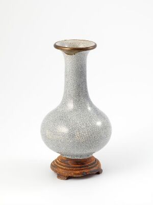  A silver-sparkle textured vase with a narrow neck and flared opening, resting on a red-brown polished wooden pedestal, set against a soft white background.