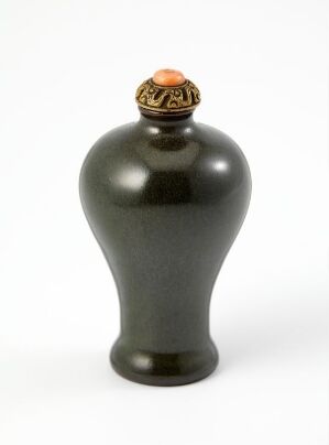  An elegant, glossy black vase with a bulbous body and ornamental lid featuring golden accents and a central stone or bead, set against a stark white background. Artist name and title are unknown.