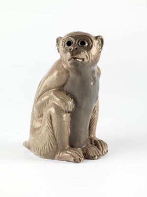  A small, sculpted figure of a seated monkey with a creamy beige color, showing textured details indicative of fur, and a focused expression with darkened eyes and mouth, set against an off-white background.