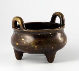  A small, glossy dark-brown ceramic pot with golden flecks, two arched handles, and three stubby legs against a light gray background.