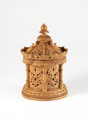  An intricately carved miniature wooden pavilion with a tiered and ornate roof, featuring detailed latticework, on a plain background.