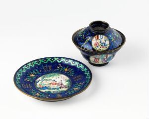  An ornate Oriental porcelain plate and covered bowl set, featuring a cobalt blue base with gold, green, and red decorative patterns, showcasing a central landscape motif on the plate.