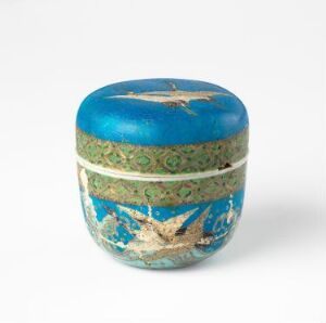  A small, circular box with a vibrant blue and gold decorative pattern, featuring a green band with gold accents around the lid, suggestive of antique or vintage craftsmanship.