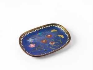  An oval-shaped decorative dish with a dark blue background and a colorful floral design featuring vibrant red, pink, yellow, and green hues, bordered by a beige trim with small details, against an off-white background.