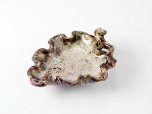  A small, wavy-edged object with a gradient of beige to brown colors suggestive of metal or ceramic, placed against a white background.