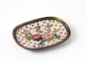  An oval-shaped ceramic dish with a creamy white background, decorated with a colorful floral pattern featuring large pink blossoms, small blue and yellow flowers, and green foliage, framed by a dark blue rim. Artist name and title are unknown.