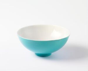  A simple ceramic bowl with a glossy two-tone design, featuring a white interior and a turquoise blue exterior, against an off-white background.