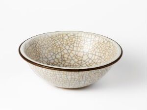  An off-white ceramic bowl with a dark rim and intricate crackle glaze pattern inside, displayed against a plain, light background.