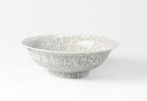  A ceramic bowl with an off-white base color and a fine grey crackled pattern throughout, on a white to light grey gradient background.