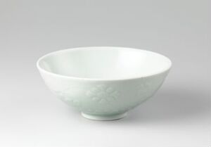  An elegant pastel green ceramic bowl with a flared rim and a subtle embossed floral pattern on its side, reflecting gentle light on its glossy surface.