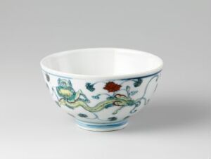  A Chinese porcelain bowl on a light grey background, featuring painted blue dragons adorned with red and green accents on a white porcelain surface, with a blue-rimmed lip.