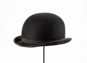  A classic black bowler hat with a rounded crown and a short, upturned brim, displayed against a neutral background on an inconspicuous stand.