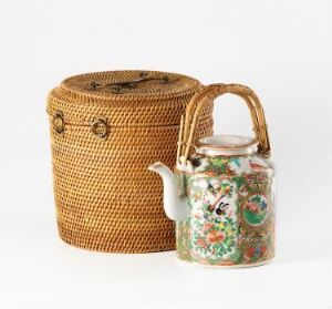  A golden brown woven basket with a lid next to a glossy porcelain teapot with an intricate floral design on a light gray background.