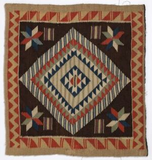  A handmade square quilt piece featuring a symmetrical, geometric design with concentric diamonds in shades of brown, red, cream, blue, and indigo, with flower-like motifs at each corner on a deep brown background, exhibiting a warm, earthy color palette.