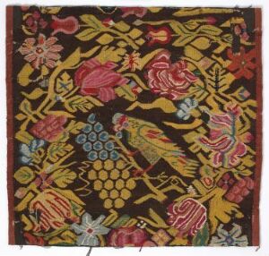 
 A textile featuring a complex pattern with peacocks and botanical motifs in red, yellow, and green on a black background. Artist name and title are unknown.