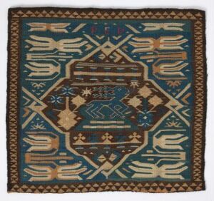  A traditional square textile featuring a symmetrical pattern with a central diamond-shaped medallion in dark blue filled with cross-shapes and floral designs in lighter blue and beige, surrounded by borders with beige feather-like motifs and an outermost brown geometric pattern on a consistent dark blue background.