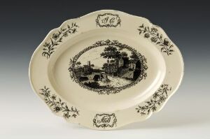  Antique oval ceramic plate with intricate black pastoral design on a white background, featuring a detailed central landscape scene and symmetrical floral motifs around the border.