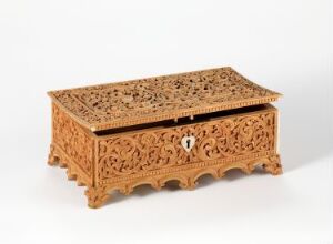  An intricately carved wooden chest with a flat top and elaborate openwork designs, resting on a neutral surface against a simple, light background.