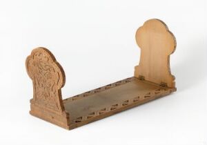  A wooden daybed with classic design influences, featuring a flat plank base and two elegantly carved arched end pieces. The wood is light brown with a natural finish, showcasing the wood's grain. The daybed is presented against a neutral backdrop with soft lighting. Artistname and title are unknown.