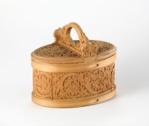  An ornately carved oval wooden box with a hinged lid and a handle on a light background, displaying intricate floral scrollwork patterns around its sides and on the top.