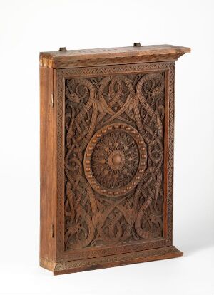  An antique wooden cabinet or panel with elaborate carvings, featuring a central medallion with ornate patterns, bordered by swirling interlocking designs, with a warm brown color.