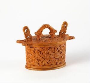  A small terracotta-colored container with intricate carvings and a central, intertwined loop handle flanked by two smaller side handles, against a white background. Artist name and title are unknown.