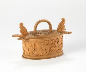  An intricately carved light brown wooden container with decorative handles on the sides and a matching carved lid handle, set against a plain white background.