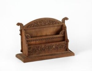  A small, intricately carved wooden bench with a high, decorative backrest featuring floral and foliate motifs, standing on a flat base with ornamental finials at each end.