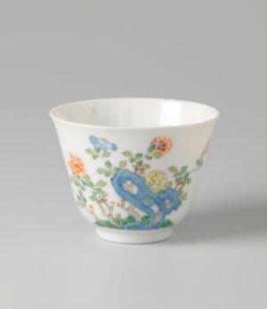  An elegant porcelain bowl with a white or cream background, adorned with colorful hand-painted flowers in shades of orange, red, and pink, and featuring a prominent cobalt blue decorative symbol or monogram integrating with the floral pattern, set against a neutral backdrop.