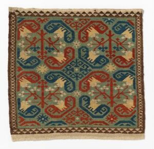  An image of an ornate textile featuring geometric and stylized floral patterns in dark teal, deep red, beige, and pale blue, surrounded by an intricate border of repeating red and beige geometric shapes.