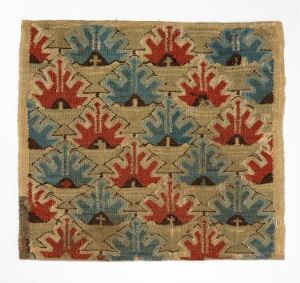  A handwoven pillow cover titled "Skybragd" by an unidentified artist, kvinner, featuring geometric motifs in deep reds, dark blues, and muted greens on a natural unbleached linen background. The hand-spun wool yarn displays plant-dyed colors, arranged in repetitive patterns suggestive of stylized flora or sunbursts, framed within a harmoniously woven grid structure. The craftsmanship reflects traditional weaving techniques and Nordic aesthetic influences.