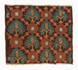  A square textile featuring a symmetrical pattern with octagons in brown, teal, and blue, displaying stylized plant motifs inside each shape, set against a warm rusty brown background with frayed edges.