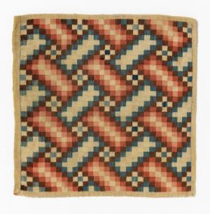  Square textile with a three-dimensional geometric pattern in muted beige, red, blue, and black colors, slightly frayed at the edges, suggesting an aged or worn material.