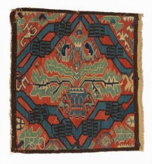  An intricately patterned square textile with a symmetrical design, featuring a color palette of teal, navy blue, terracotta, muted green, burnt orange, and beige, showing signs of aging and fraying at the edges.