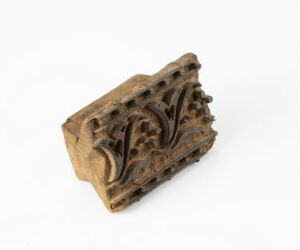  A small, intricately carved object with a brown, earthy tone, possibly a piece of historic architectural ornamentation, on a light gray background.