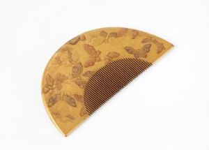  A semi-circular, fan-shaped object with a golden-yellow background featuring illustrations of animals and plants in a slightly darker shade. The lower half displays a ribbed texture with vertical, parallel lines in a darker brown color, against a plain white background.