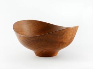  A wooden bowl with an artistic and asymmetrical design, presenting a rich honey-brown color and a natural wood grain pattern, set against a pure white background.