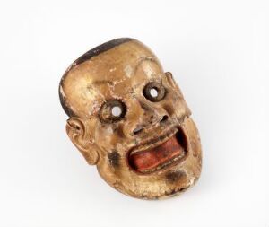  An intricate Noh mask with a gilded, expressive face featuring wide eyes, arched eyebrows, and an open mouth against a white background. The craftsmanship includes carved facial features, worn gilding, and a blend of golden, black, and red hues.