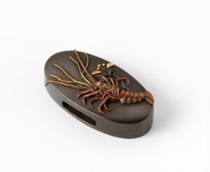  A finely detailed, small brown and gold lobster netsuke with a flat oval base situated against a plain white background. The object is carved with precision, showcasing the lobster's segmented anatomy and textured surface.