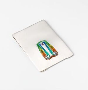  A small rectangular silver writing accessory designed by Archibald Knox with rounded corners and a central decorative inlay of vivid green, orange, and royal blue enamel in an elongated symmetrical motif on a plain background.