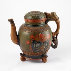  An antique olive green teapot with red floral patterns and gold accents, a brown handle, and three rounded feet. The aged finish suggests it's a vintage item, possibly handcrafted.