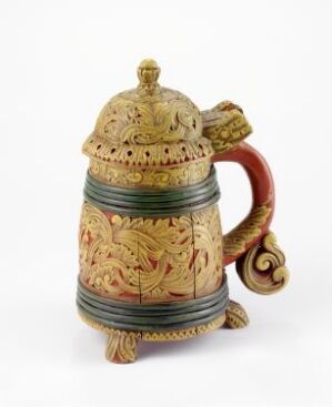  A decorative teapot with an olive green base color and intricate yellow, orange, and soft red floral designs, a burgundy handle with golden accents, and a crowned-like finial on the lid, set against a plain white background. The artist's name and title are unknown.