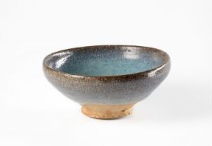  A shallow ceramic bowl with a glossy blue glazed interior that transitions to lighter blue at the edges. The outer surface displays a gradient from brown to speckled grey, finishing with a natural, unglazed terra cotta base on a white background.