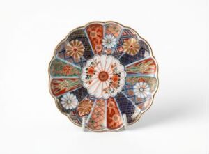  Decorative round plate with a symmetrical and colorful pattern, featuring a central floral motif in white, red, and blue, surrounded by alternating dark blue and orange segments with detailed floral patterns, all edged with a fine white outline.