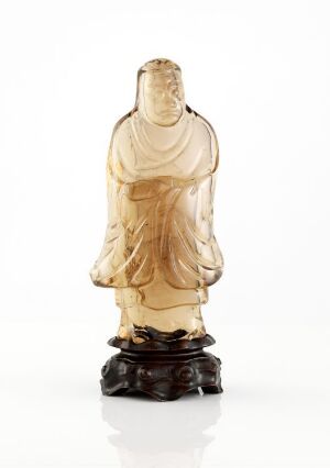  A translucent, amber-colored statuette of a dignified figure in flowing robes stands on a dark base against a plain white background. The sculpture has an ethereal quality due to the play of light through its material.