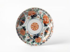  An ornately decorated ceramic plate with a centered stylized citrus motif surrounded by a complex pattern of flowers in blues, oranges, and greens, indicating a traditional or classical design. The artist name and title are unknown.