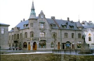  A historic stone building with a spire-topped turret on the right, arched windows, and a conical turret roof set against a gray overcast sky. The structure's sophisticated design suggests European architectural influences from the late 19th or early 20th century.