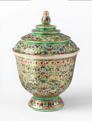  An intricate "Tho song Koth" porcelain lidded jar with a detailed, enamel painted garden design in shades of green with red, blue, yellow, and pink accents, on a white background. The jar has a rounded body, a matching lid with a small finial, and sits on a pedestal-like base.