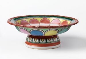  A Bencharong porcelain dish with a vibrantly painted design featuring a pattern of alternating red, green, yellow, and blue half-circles, outlined in black on a white glossy background. The dish has a shallow bowl and a flared rim, set on a small-footed base. Artist name is unknown.